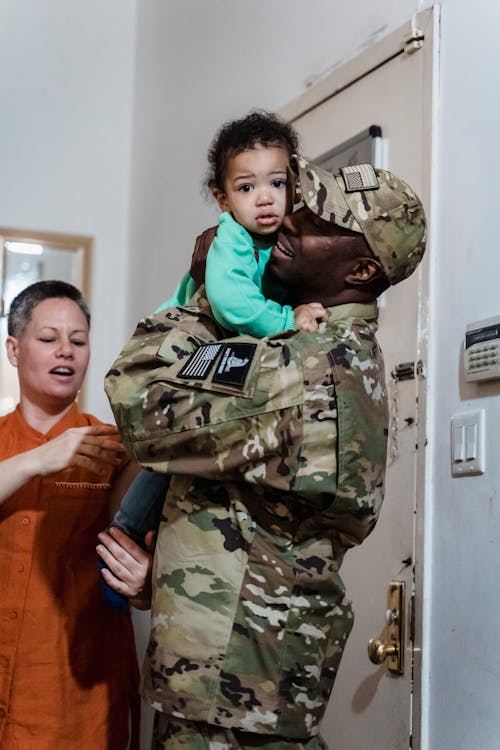 A Man in Military Uniform Carrying a Kid in Green Long Sleeve Shirt