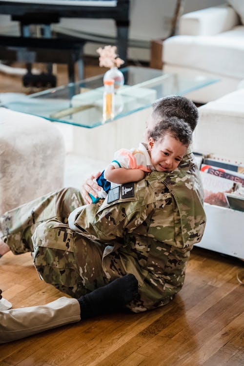 A Soldier Carrying a Child while Sitting on Wooden Flooring