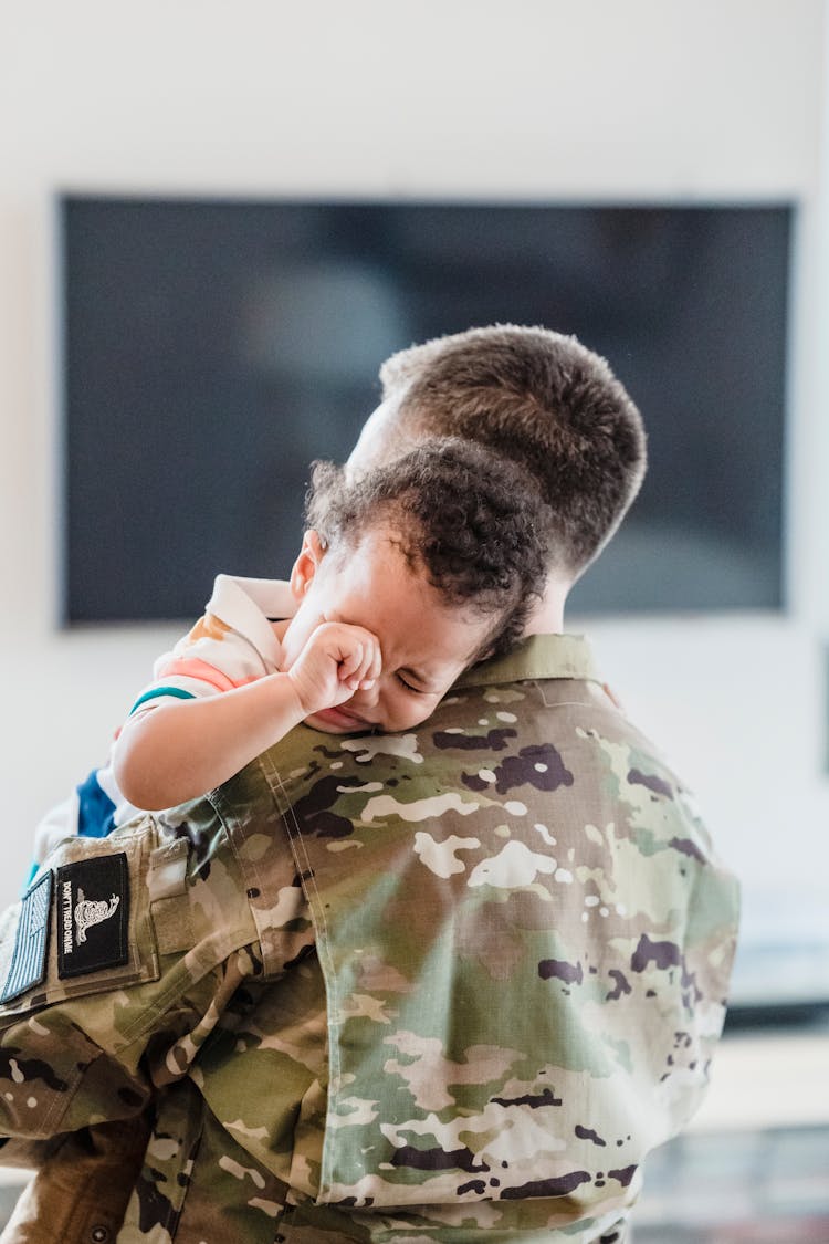 A Person In Military Uniform Carrying A Child Crying