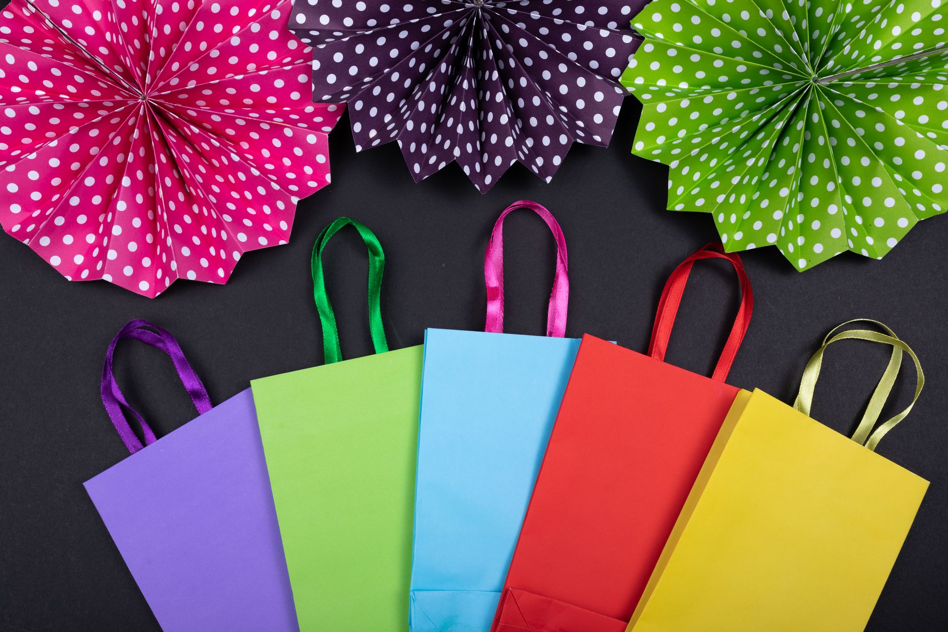 Vibrant flat lay of colorful shopping bags and polka dot decorations on a black background.
