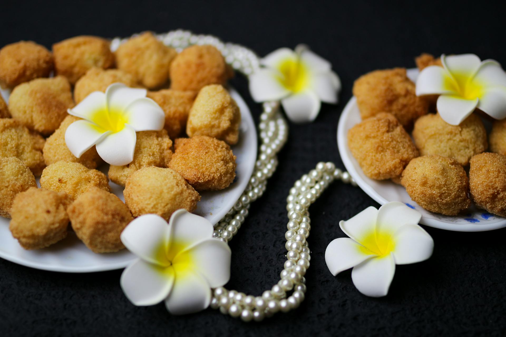 Plate of golden croquettes beautifully decorated with white and yellow plumeria flowers and pearls.