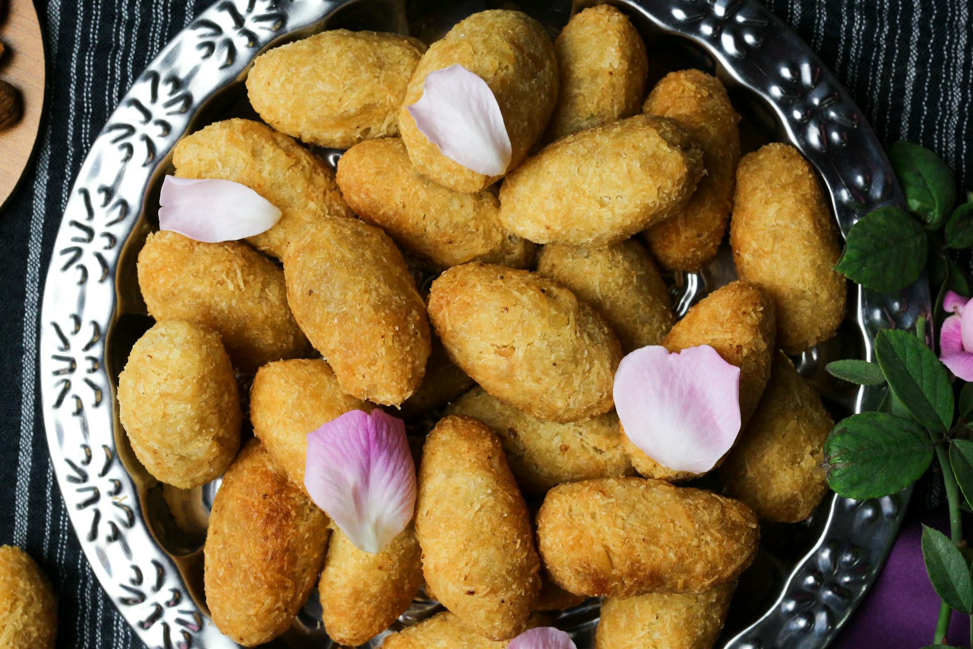 Delicious golden brown croquettes garnished with pink petals on a decorative tray.