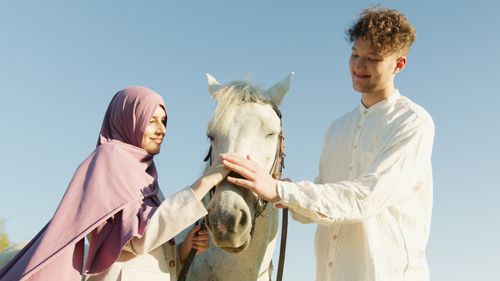 Free A young couple warmly interacting with a white horse in a sunny outdoor setting. Stock Photo