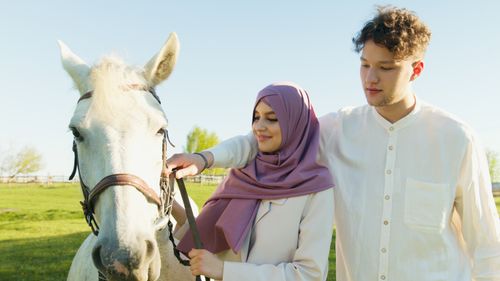 Free A couple enjoying a sunny day outdoors with a white horse, showcasing love and togetherness. Stock Photo