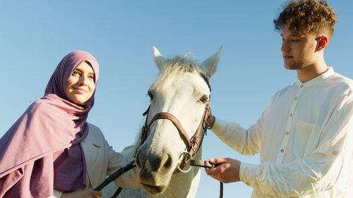 Free Gentle interaction between a couple and a white horse under a clear blue sky in the countryside. Stock Photo