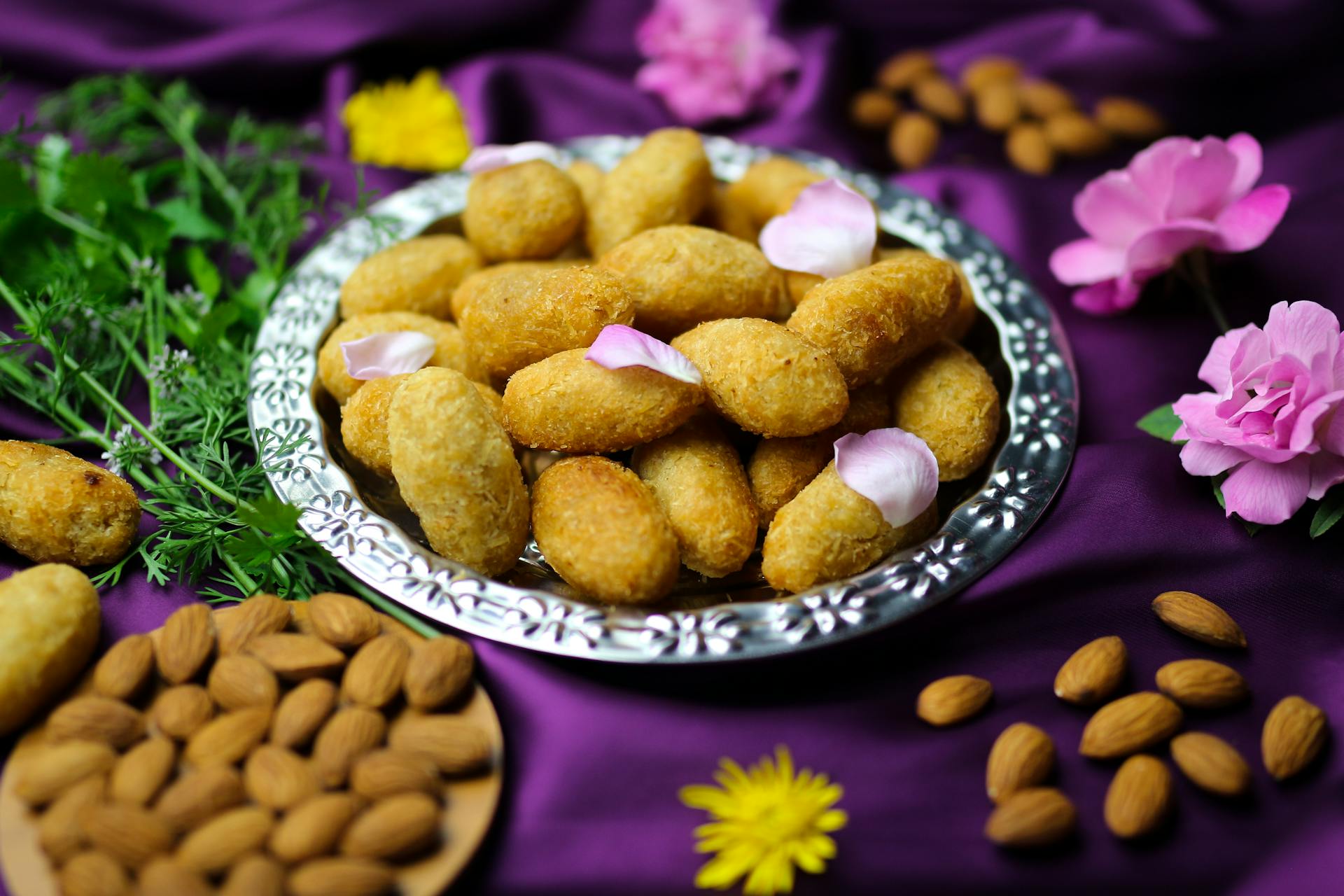 Stylish display of croquettes on a silver platter, garnished with flower petals and almonds.