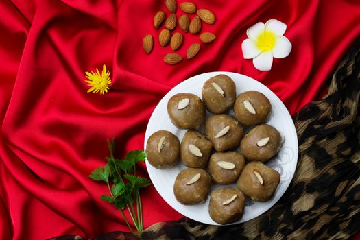 A plate of almond pastries on vibrant red silk with flowers and herbs.