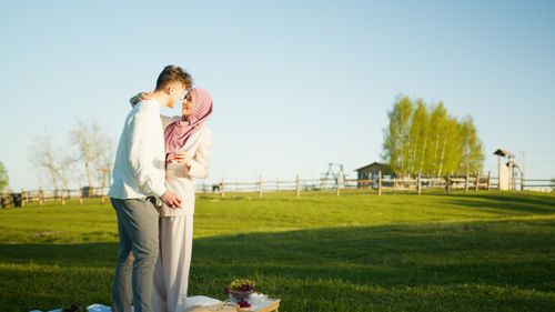 Free A couple shares a tender moment during a picnic on a sunny day in a lush green meadow. Stock Photo