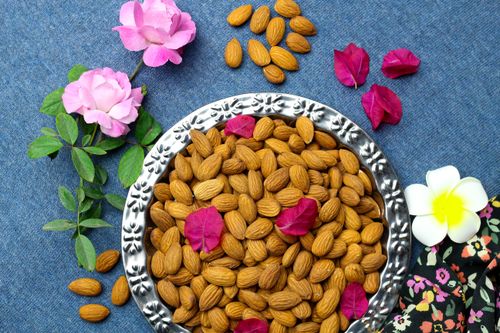 Free Charming still life featuring almonds in a bowl surrounded by vibrant flowers on a blue background. Stock Photo