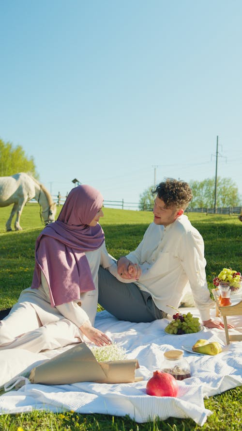 A Couple Sitting on a Picnic Blanket while Holding Each Others Hand
