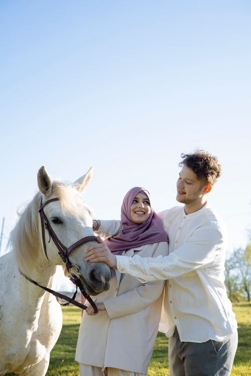 Free A couple enjoying time with a white horse on a sunny day outdoors. Stock Photo