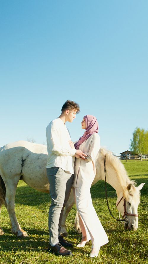 Free A loving couple stands together with a horse in a sunny countryside field. Stock Photo