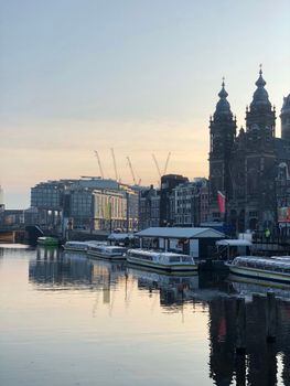 Romantic view of Amsterdam canal with boats and historic church reflection at dusk.