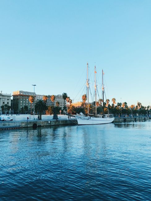 Serene view of a sailboat docked at Barcelona harbor under a clear blue sky.