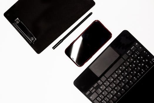 Flat lay of modern devices including a smartphone, tablet, pen, and keyboard on a white surface.