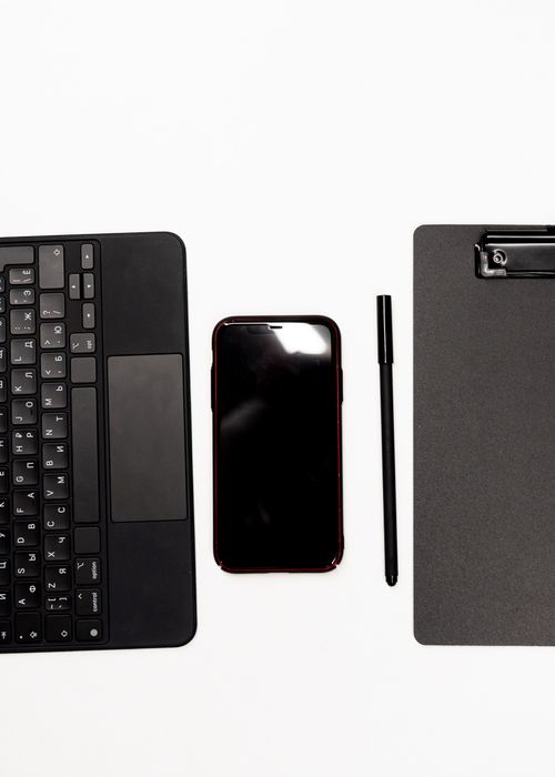Free Minimalist flat lay of a keyboard, smartphone, pen, and clipboard on a white background. Stock Photo
