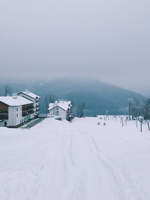 Foggy winter scene of snow-covered mountains in Sochi, Russia with residential buildings.