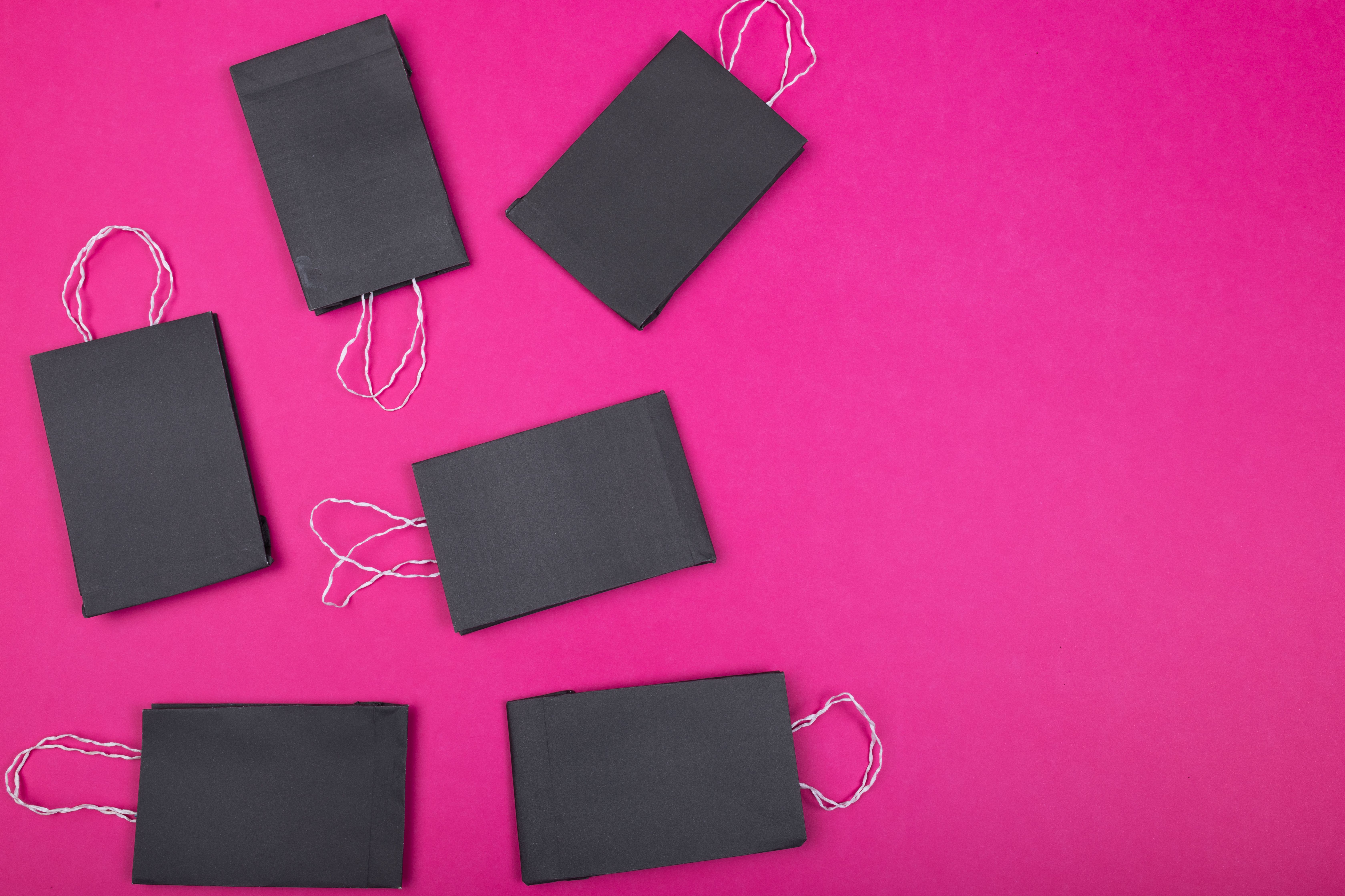 Flat lay of black shopping bags on vibrant pink background. Ideal for retail concepts.