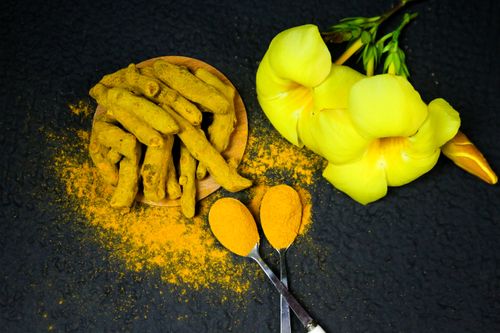 Free Close-up of turmeric roots, powder, and yellow bell flowers on a black background. Stock Photo