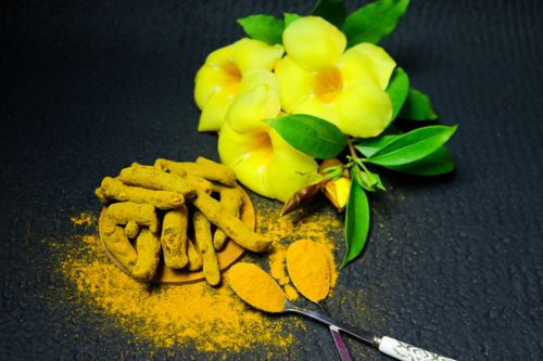 Free A vibrant display of turmeric root, powder, and yellow flowers on a textured black background. Stock Photo