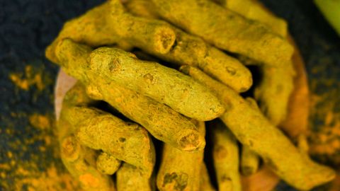 Vibrant close-up of organic turmeric roots displayed on a wooden plate, perfect for cooking and health inspiration.