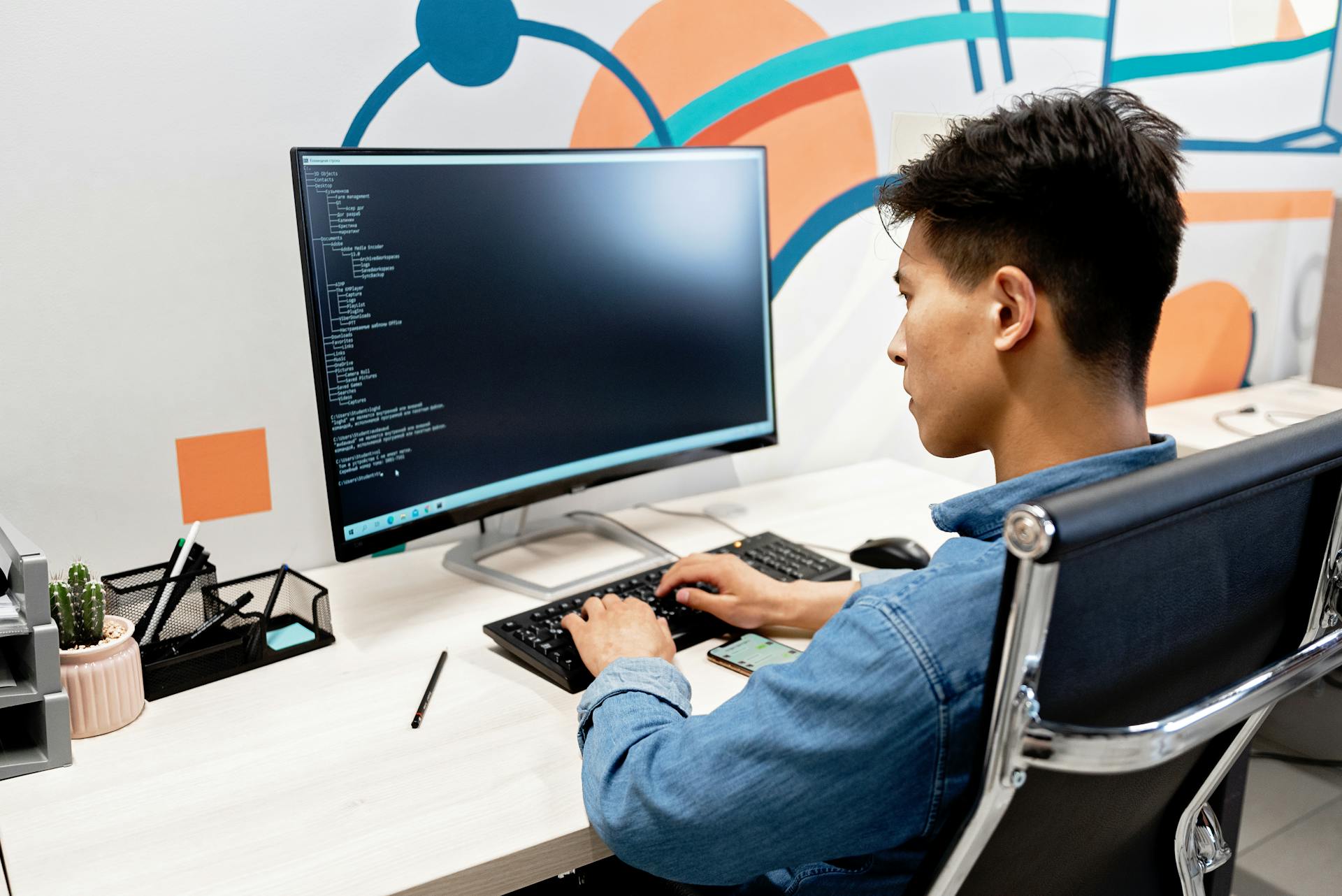 Adult male programmer working on code at a modern desk setup with a large monitor.