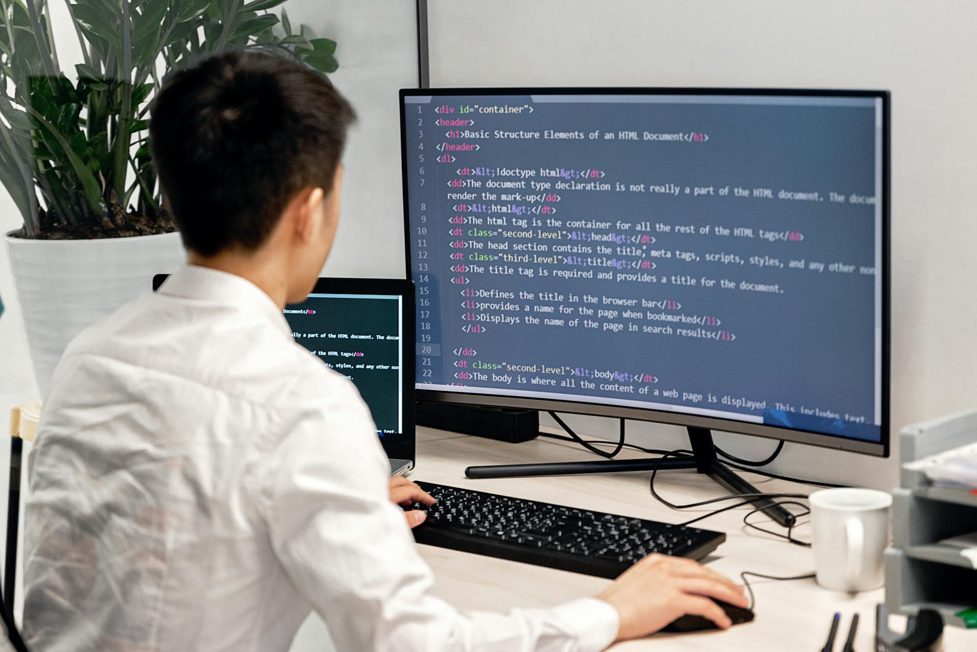 Adult male programmer coding on dual monitors in a modern indoor workspace.