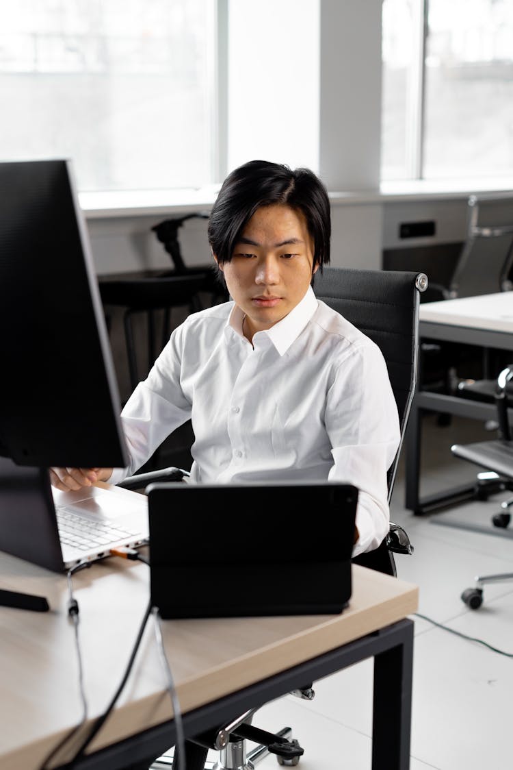 A Man Sitting On His Workspace While Looking At The Screen Of His Tablet