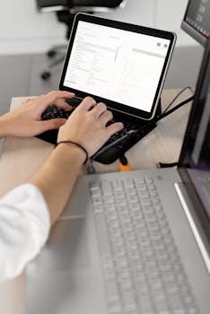 Close-up of hands typing on a laptop in an office setting, showcasing professional programming work.