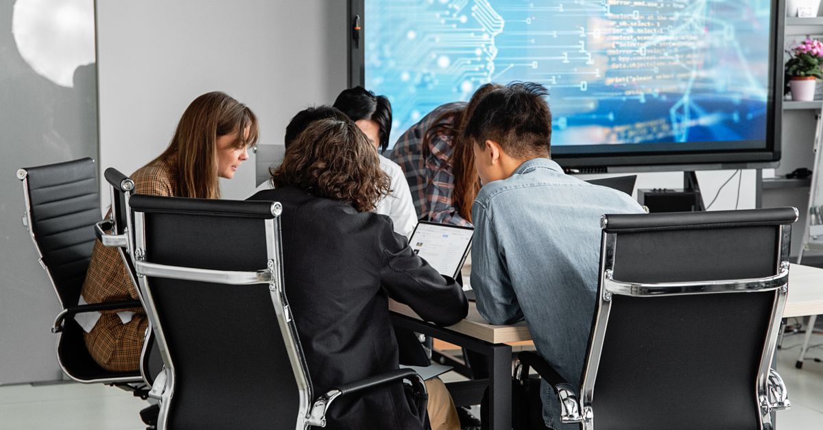 Equipo diverso de profesionales colaborando en una oficina moderna frente a una pantalla digital con datos y gráficos.