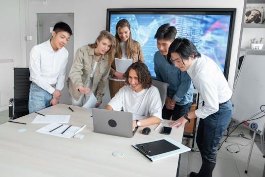 A group of young professionals actively collaborating around a laptop in a modern office setting.
