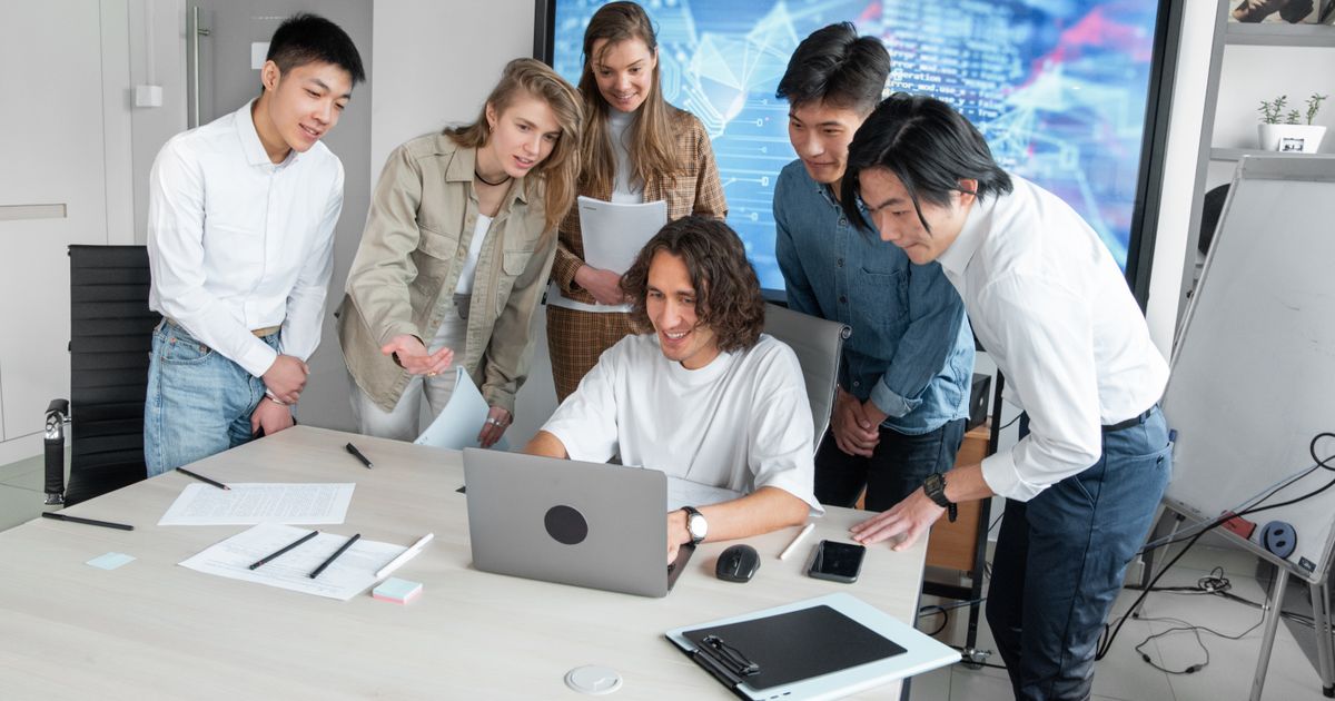 Un collaborateur montre l'écran de son ordinateur portable à des collègues réunis autour de lui dans un bureau.