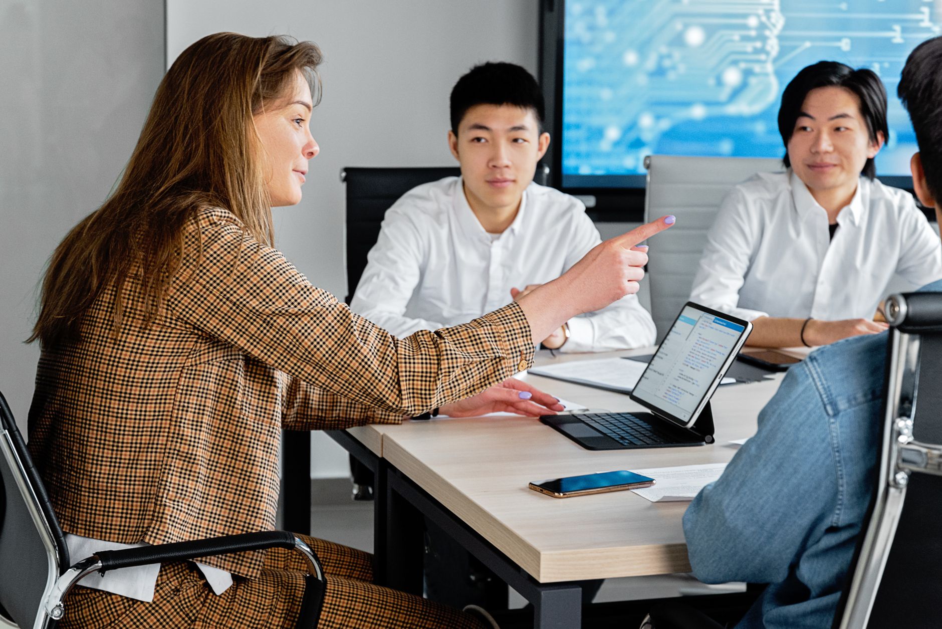 Business team collaborating around conference table with digital screens displaying AI performance dashboards risk managem...