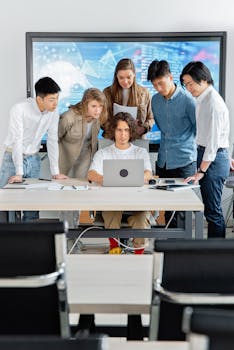 A diverse group of professionals engaged in teamwork around a laptop in a contemporary office setting.