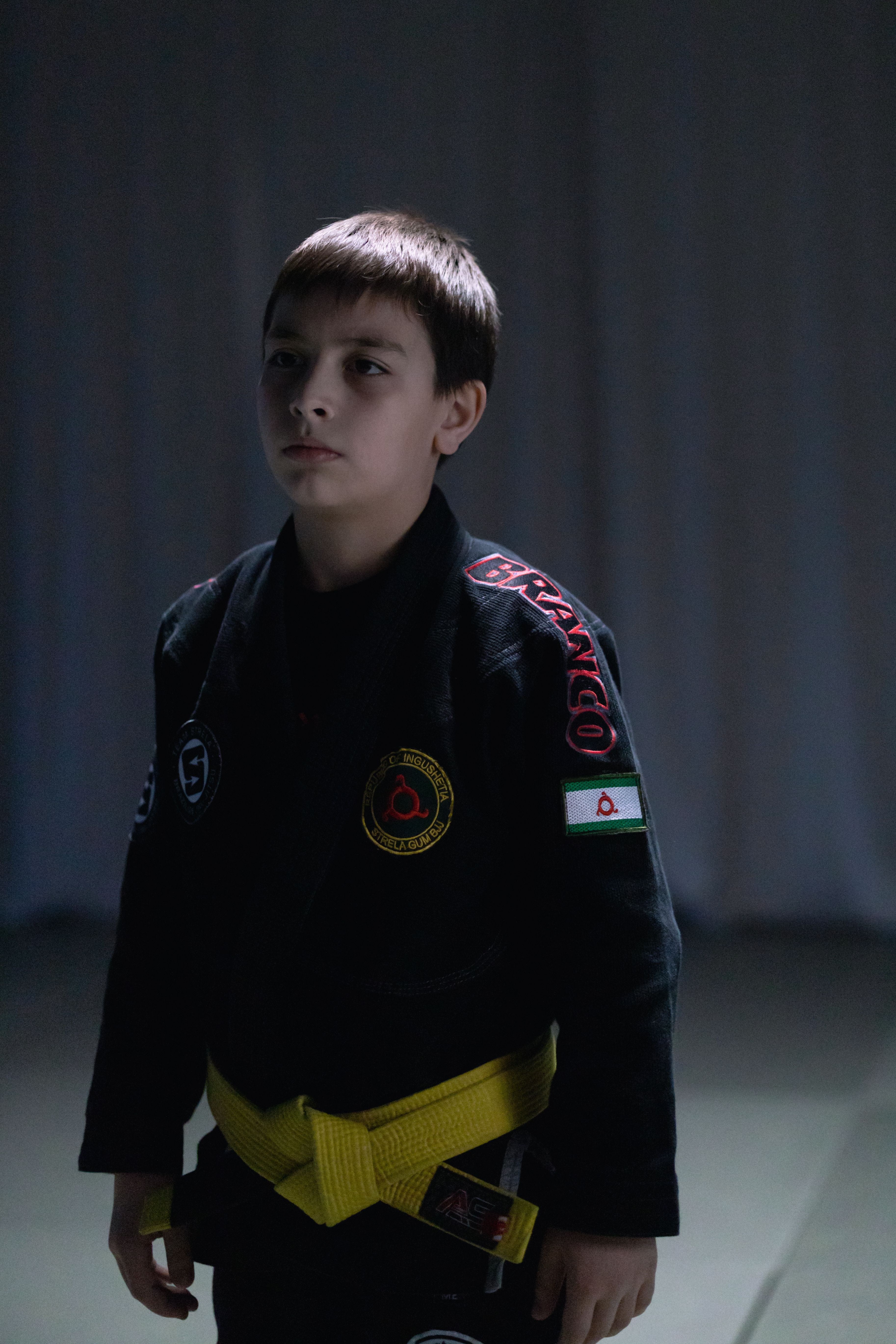A young boy in a black jiu jitsu gi with a yellow belt stands ready for training.
