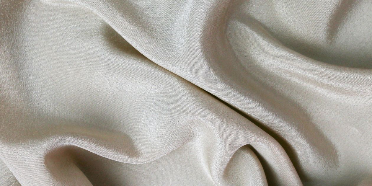 Vải màu kem với bề mặt gợn sóng mềm, minh họa độ rũ tự nhiên của satin nhẹ khi treo tự do
