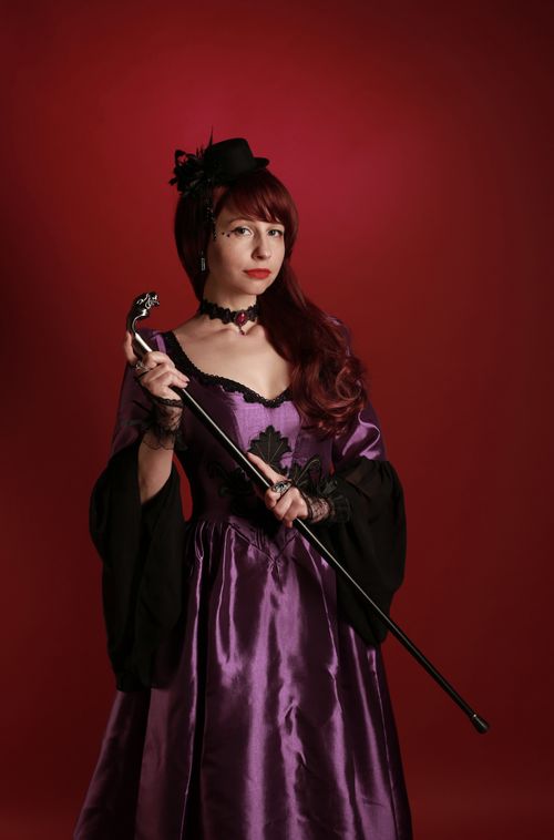Free Woman in a purple Victorian-style gown holds a cane, set against a red background. Stock Photo