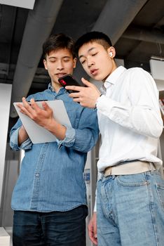 Two young men collaborating using a smartphone and clipboard in a modern office setting.