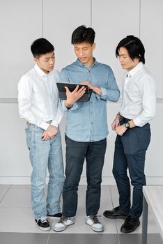 Three men collaborate on a digital tablet indoors, showcasing teamwork and discussion.