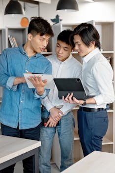 Three Asian men collaborate using digital tablets in a modern office space.