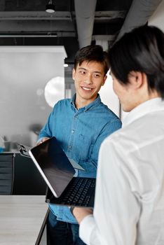 Two Asian men engaged in a collaborative discussion in a contemporary office setting.