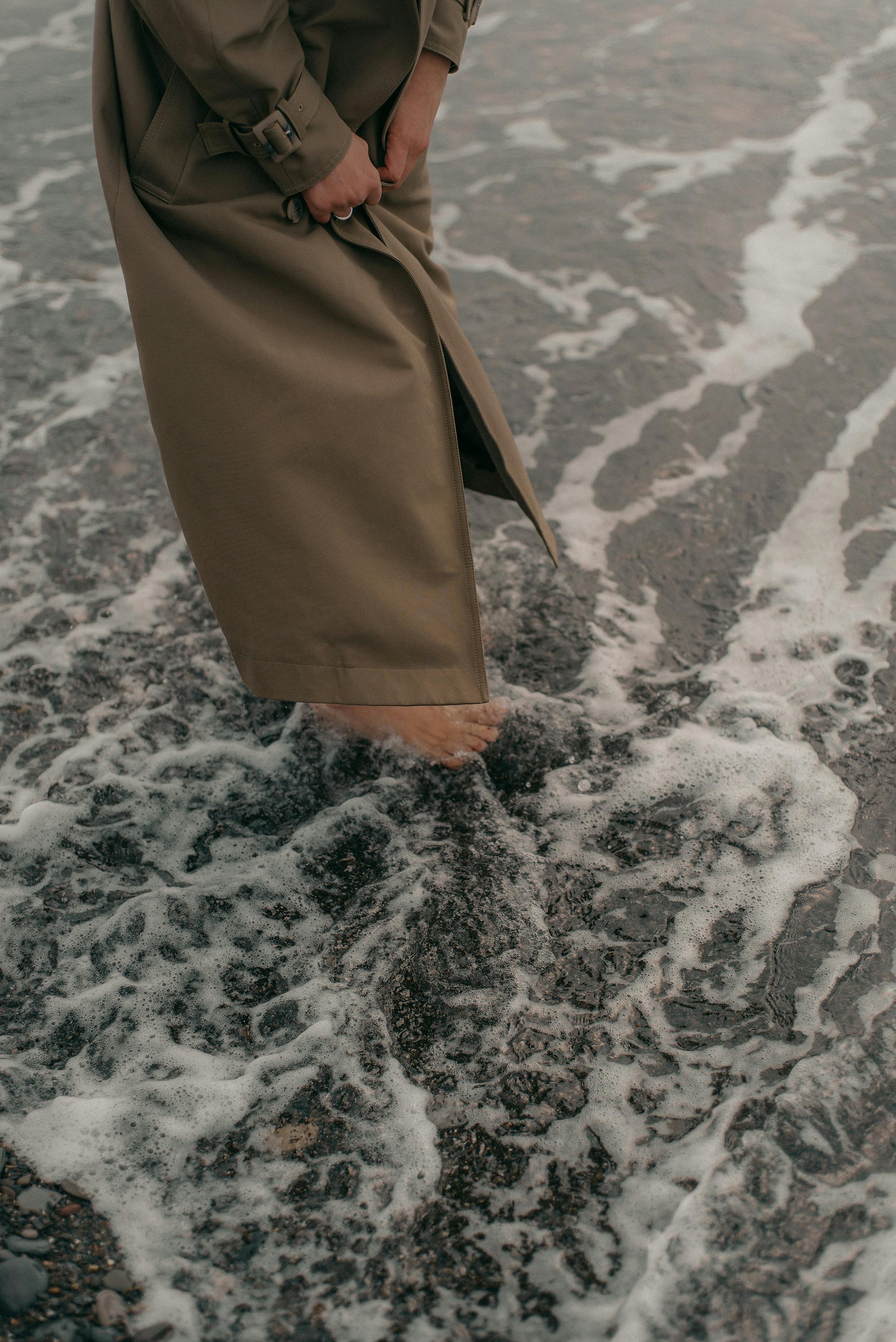 Tranquil moment of a person standing barefoot in seafoam by the shore, capturing peaceful solitude.