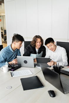 Three colleagues discuss ideas using technology devices in a modern office setting.