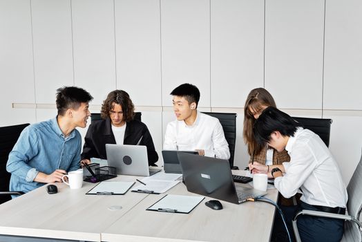 A diverse group of coworkers engaged in a productive meeting with laptops in a contemporary office.
