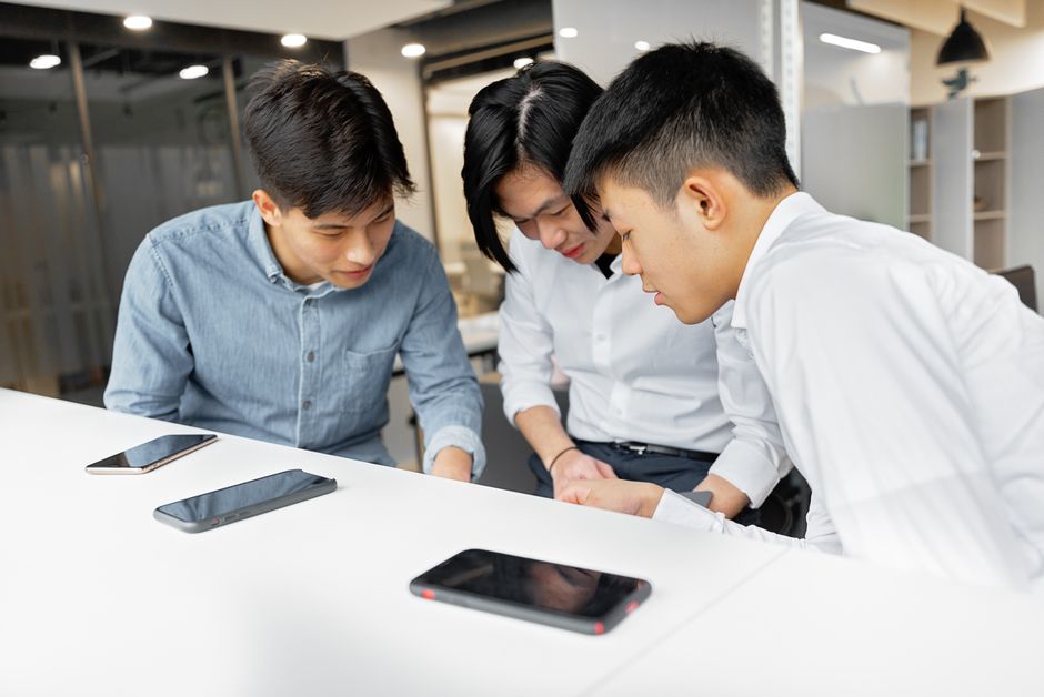 Três colegas fazendo brainstorming em um ambiente de escritório moderno, focados em smartphones.