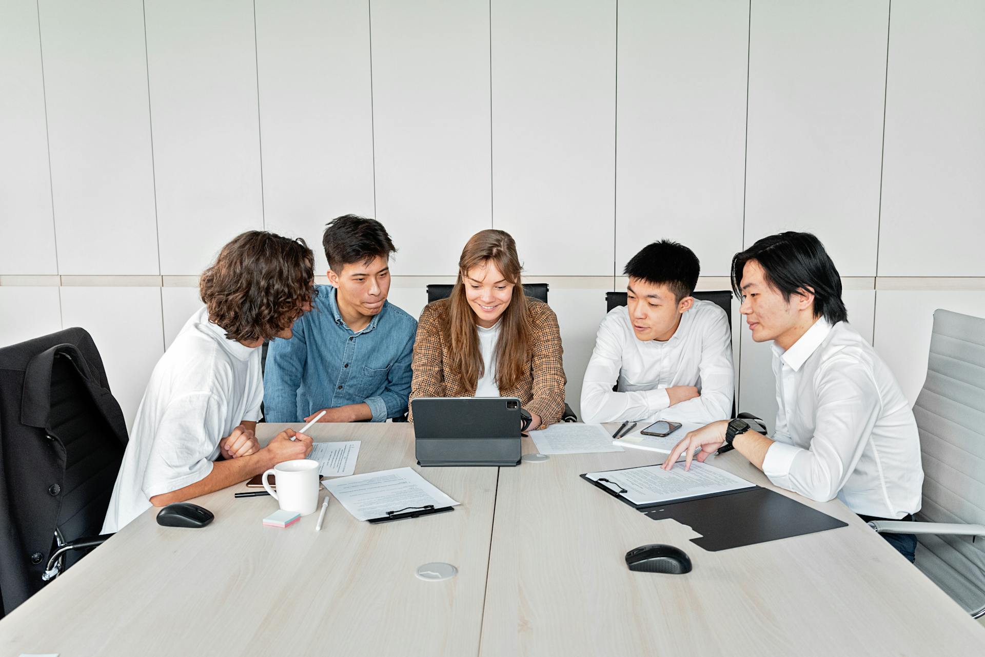 A diverse group of professionals working together around a digital tablet in a modern office setting.