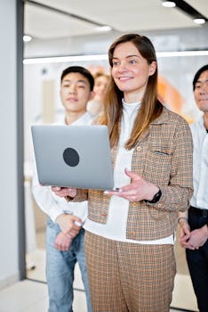 Group of young adults working together in an office setting, focused on a laptop.