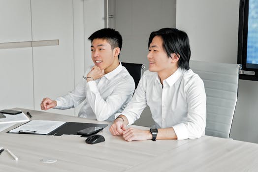 Two Asian men smiling and collaborating in a bright modern office setting.