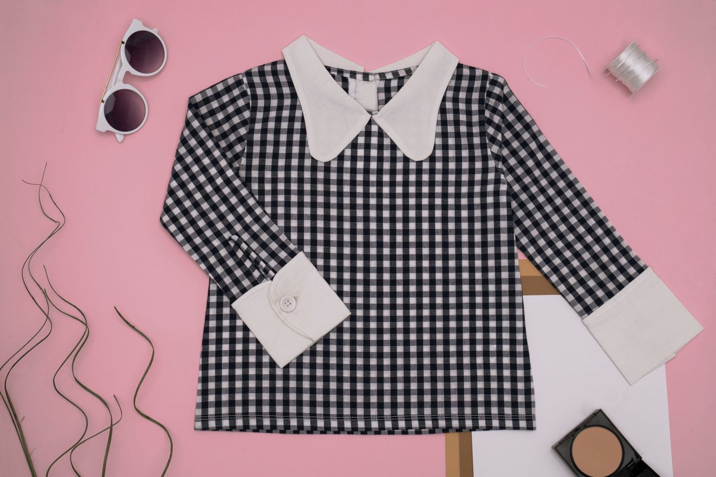 Checkered blouse and accessories arranged on a pink surface without people