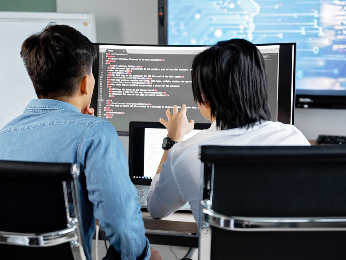 Two developers reviewing code together on a desktop monitor